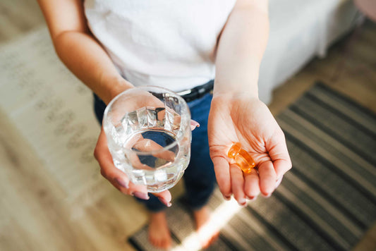 Woman holds vitamins and a glass of water in her hand
